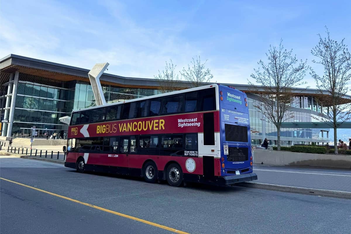 Un bus touristique à deux étages portant l'inscription "Big Bus Vancouver" est garé dans une rue de la ville, près d'un bâtiment moderne.