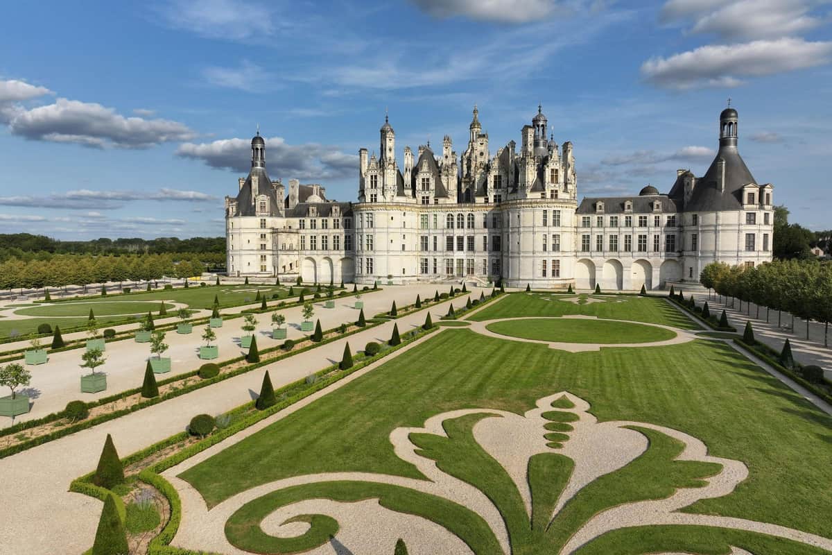 Vallée de la Loire : Excursion d'une journée avec entrée dans 3 châteaux Un grand château à l'architecture ornée, entouré de jardins manucurés, sous un ciel bleu parsemé de nuages.