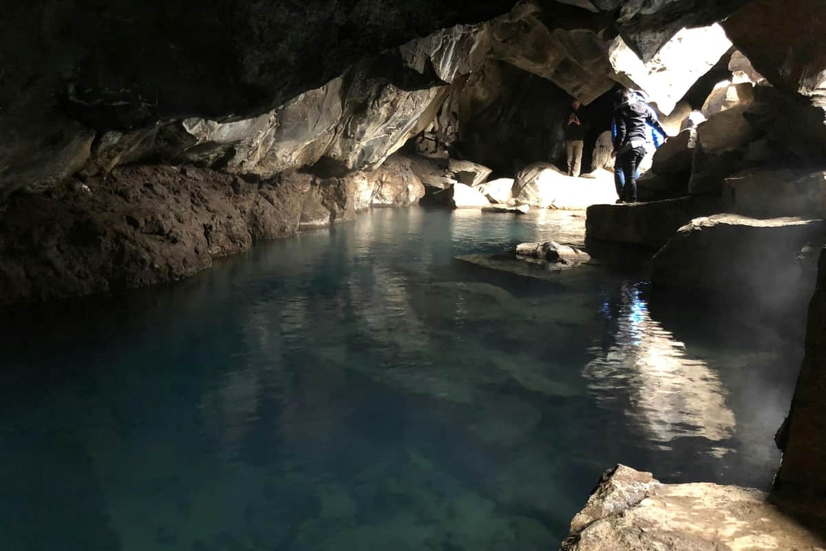 Une personne explore une grotte faiblement éclairée avec un bassin d'eau bleue claire et des formations rocheuses déchiquetées.
