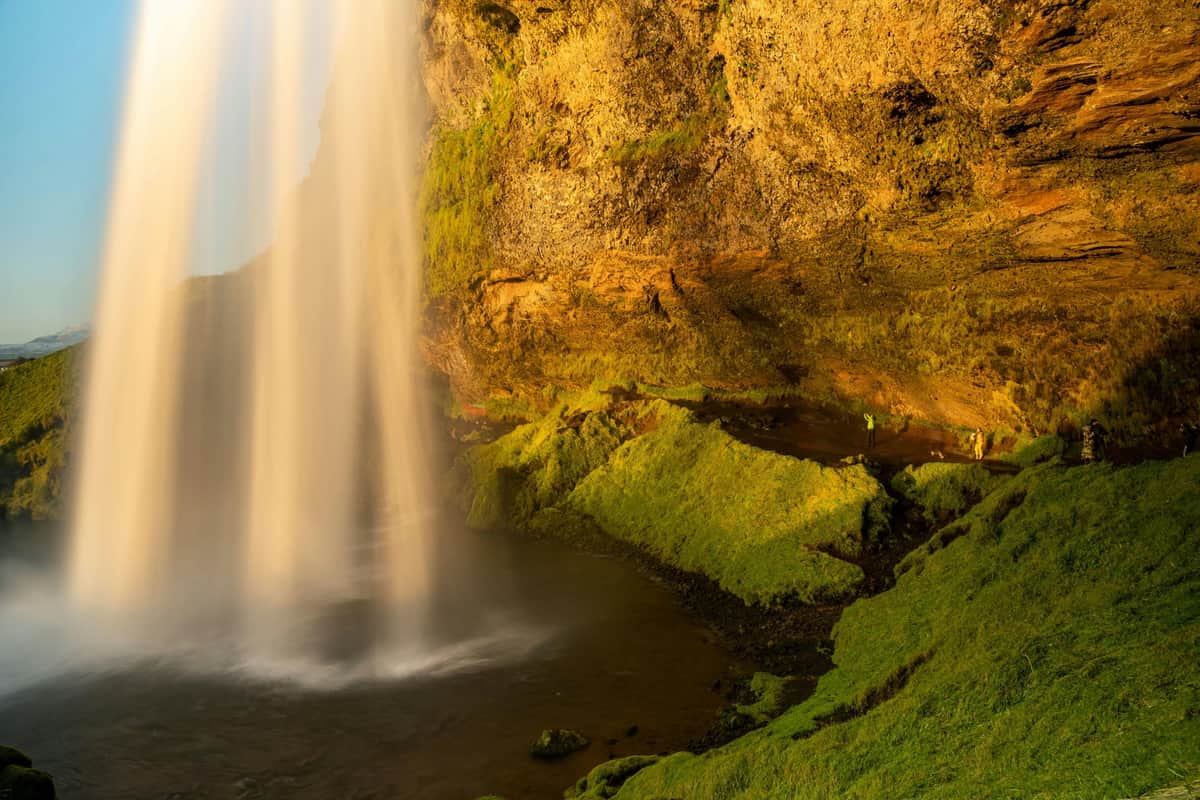 South Iceland: Bus Tour A waterfall cascades over a moss-covered cliff, with sunlight illuminating the scene.