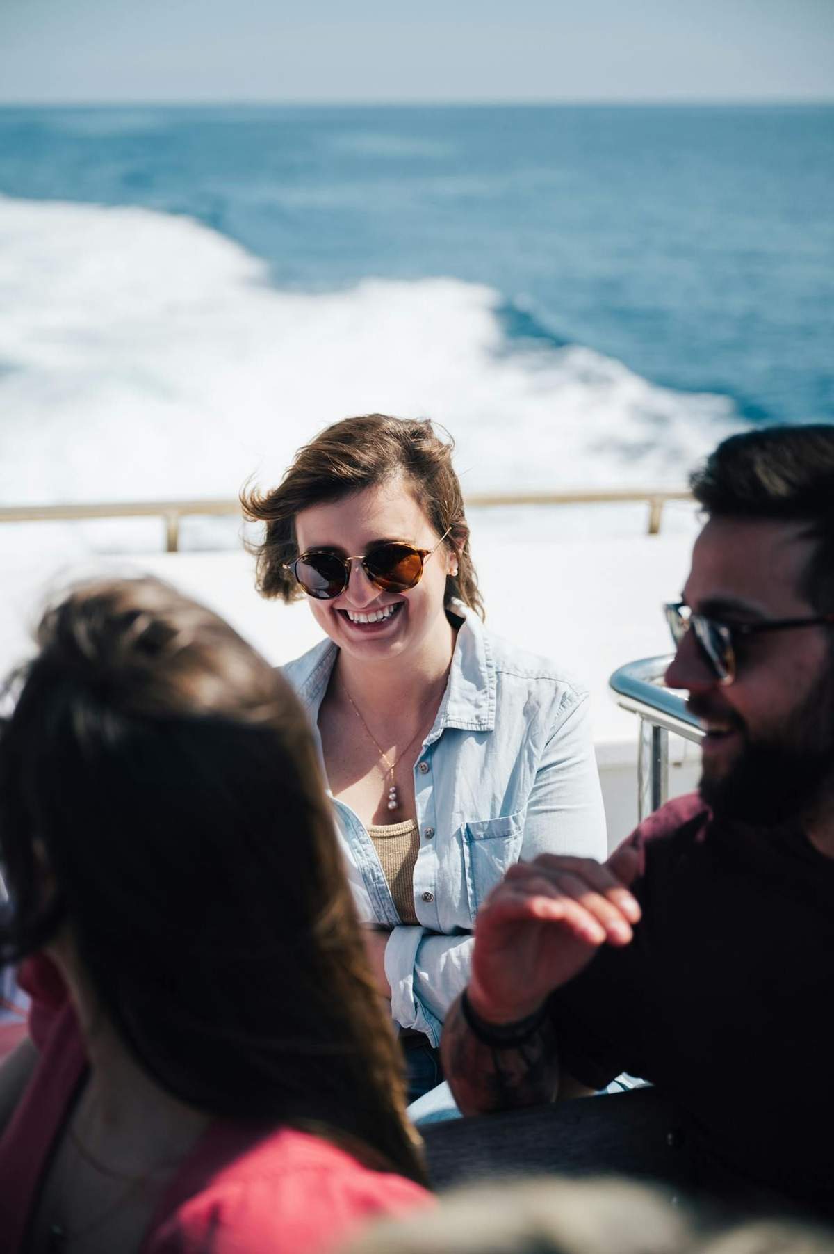 Tres personas disfrutan de un paseo en barco, dos de ellas sonrientes y con gafas de sol. El océano se ve al fondo.