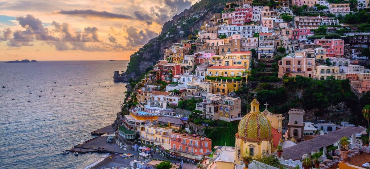 Colorful buildings on a hillside by the sea at sunset, with a gold-domed church in the foreground.