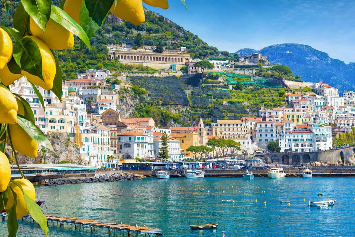 Un pintoresco pueblo costero con edificios de colores en la ladera de una colina, un mar azul claro y limones colgando en primer plano.