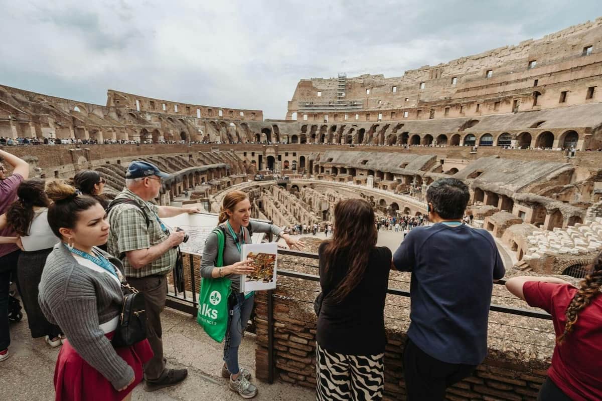 Des touristes admirent l'intérieur du Colisée à Rome, accompagnés d'un guide qui leur donne des explications tout en tenant une carte.