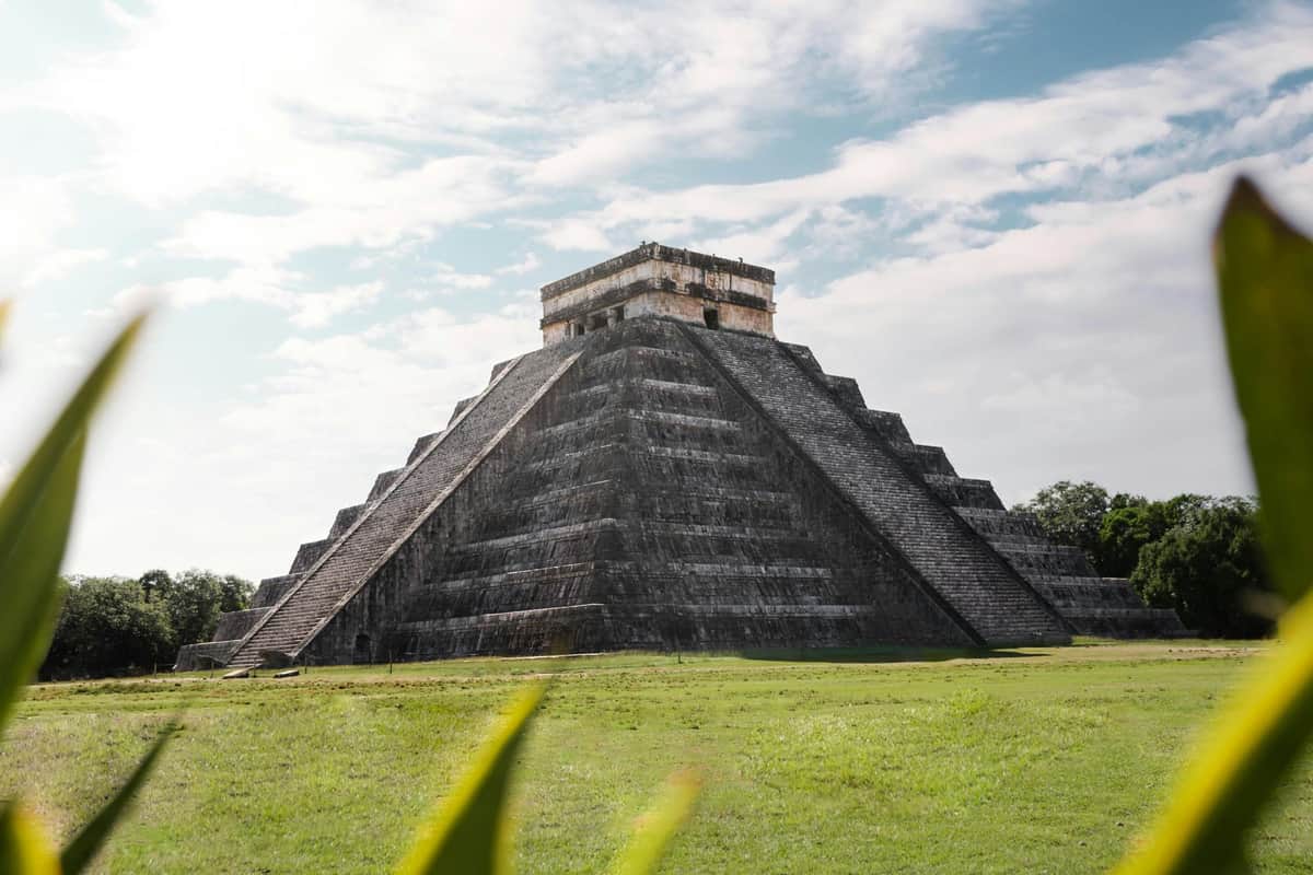 Chichén Itzá, Cobá, Valladolid y Cenote: Excursión de un día desde la Riviera Maya + Comida (Ciudad de México) Una gran pirámide de piedra antigua con una escalinata, sobre un cielo azul con nubes dispersas, rodeada de hierba verde.