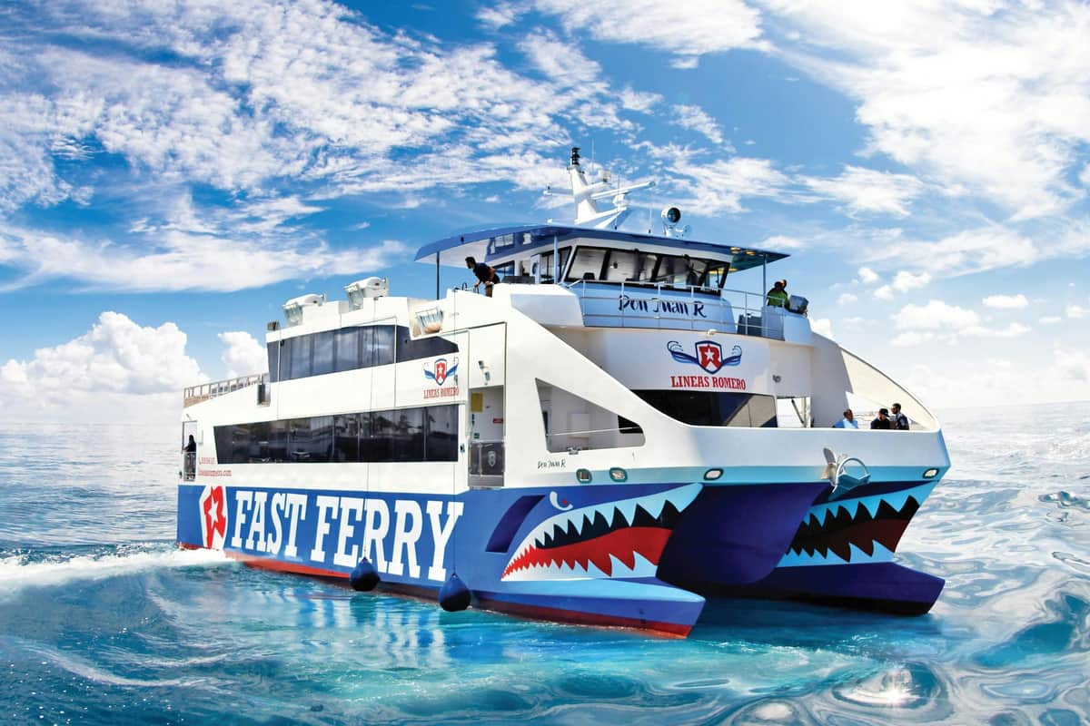 Lanzarote: Guided Tour from Fuerteventura + Wine Tasting A white ferry with "FAST FERRY" and shark mouth designs on the hull on a clear, sunny day.