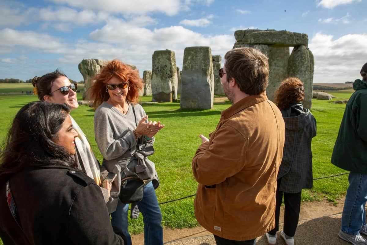 Un groupe de personnes qui discutent et sourient en plein air près de Stonehenge, par une journée ensoleillée.