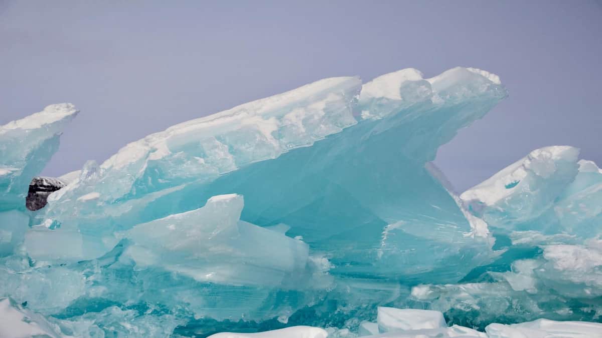 Ein großes Stück blaues Eis mit gezackten Kanten vor einem hellen, bewölkten Himmel.