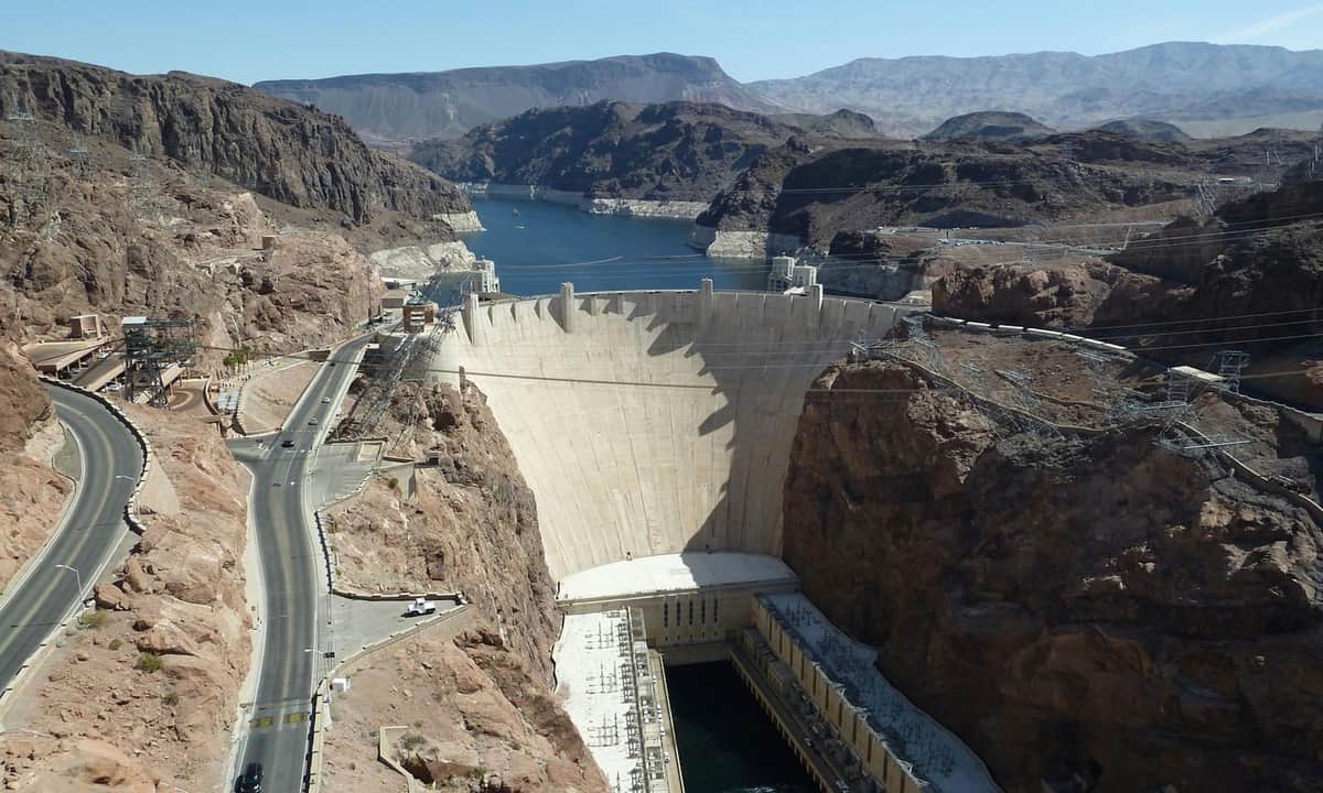 Ghost Town Explorer: Excursión desde Las Vegas Una gran presa que atraviesa un cañón con agua detrás, rodeada de terreno rocoso y carreteras. Al fondo se ven montañas.