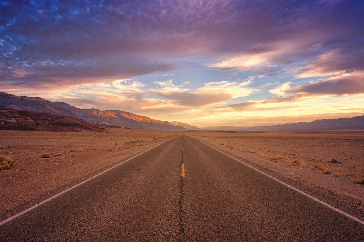 Las Vegas: excursión de ida desde Los Ángeles + entrada al Parque Nacional del Valle de la Muerte Una carretera recta se extiende hasta el horizonte a través de un paisaje desértico, con nubes espectaculares y montañas bajo un cielo lleno de colores.