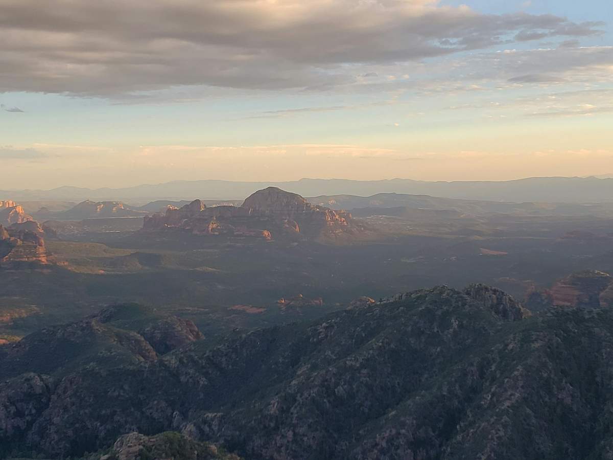 Parc national du Grand Canyon & Sedona : excursion depuis Phoenix/Scottsdale Paysage montagneux avec des pics rocheux, une mesa lointaine et un ciel rempli de nuages pendant le coucher du soleil.