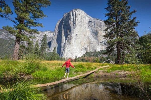 Un couple est assis sur un mur de pierre, se souriant l'un à l'autre, avec un paysage montagneux et une vallée en arrière-plan.