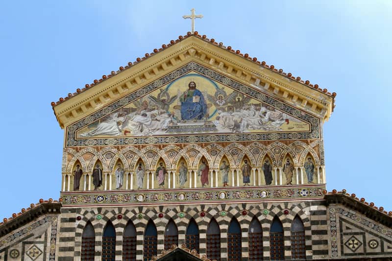 A detailed church facade with a mosaic depicting a religious scene, numerous arches, and ornate decorations under a clear sky.