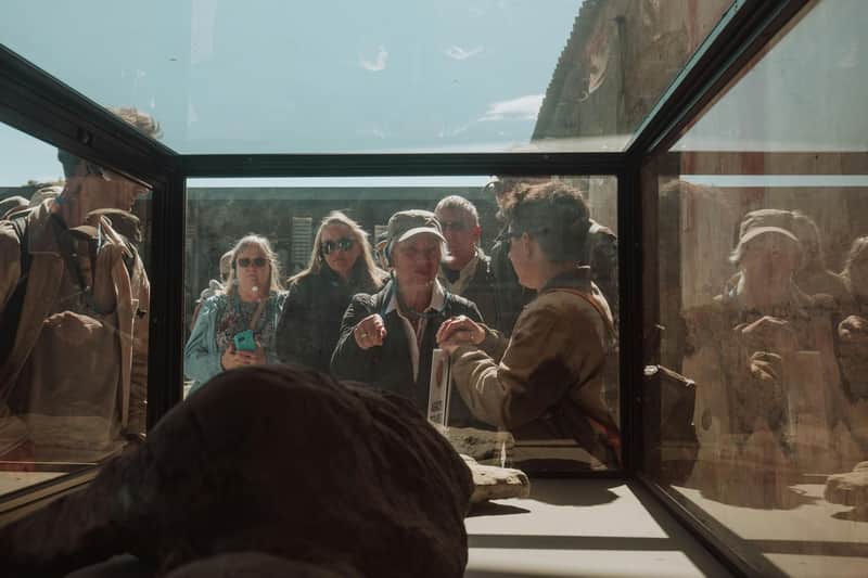 A group of people standing outdoors, viewed through a glass enclosure containing an object in the foreground.