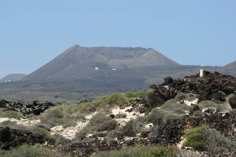 Distant view of a mountain with a flat summit and dry vegetation in the foreground, under a clear blue sky.
