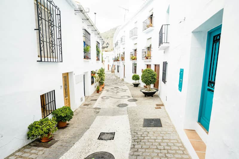 Nerja & Frigiliana: Guided Tour from Granada A narrow, cobblestone street lined with white buildings, potted plants, and wrought iron balconies, leading up a slight hill.
