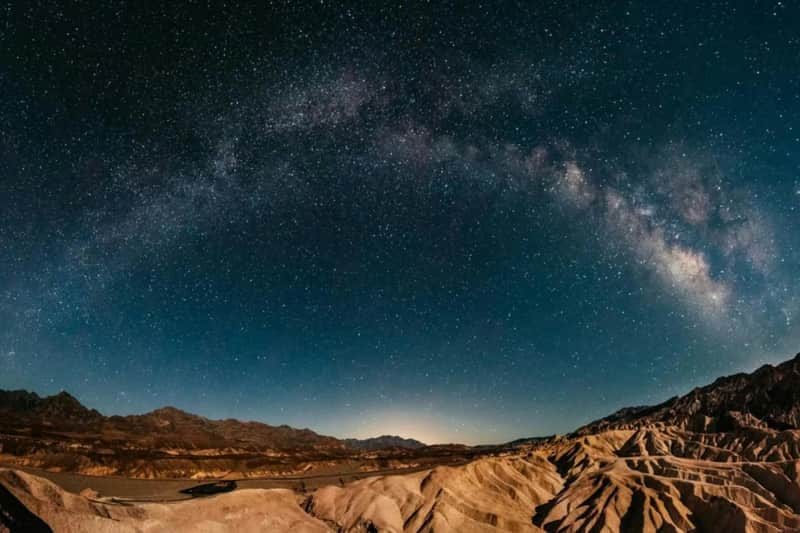 Vista notturna panoramica di un paesaggio desertico con la Via Lattea che si snoda nel cielo scuro e costellato di stelle.
