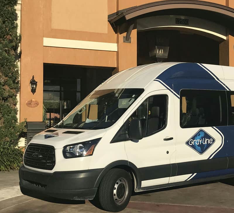 A white van with "Gray Line" branding is parked in front of a building with a large arched entrance and the number 12655.