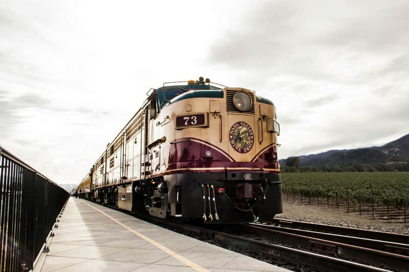 一列编号为73的老式火车，名为“纳帕谷葡萄酒火车” （ Napa Valley Wine Train ） ，在多云的天空下，毗邻葡萄园的轨道上。